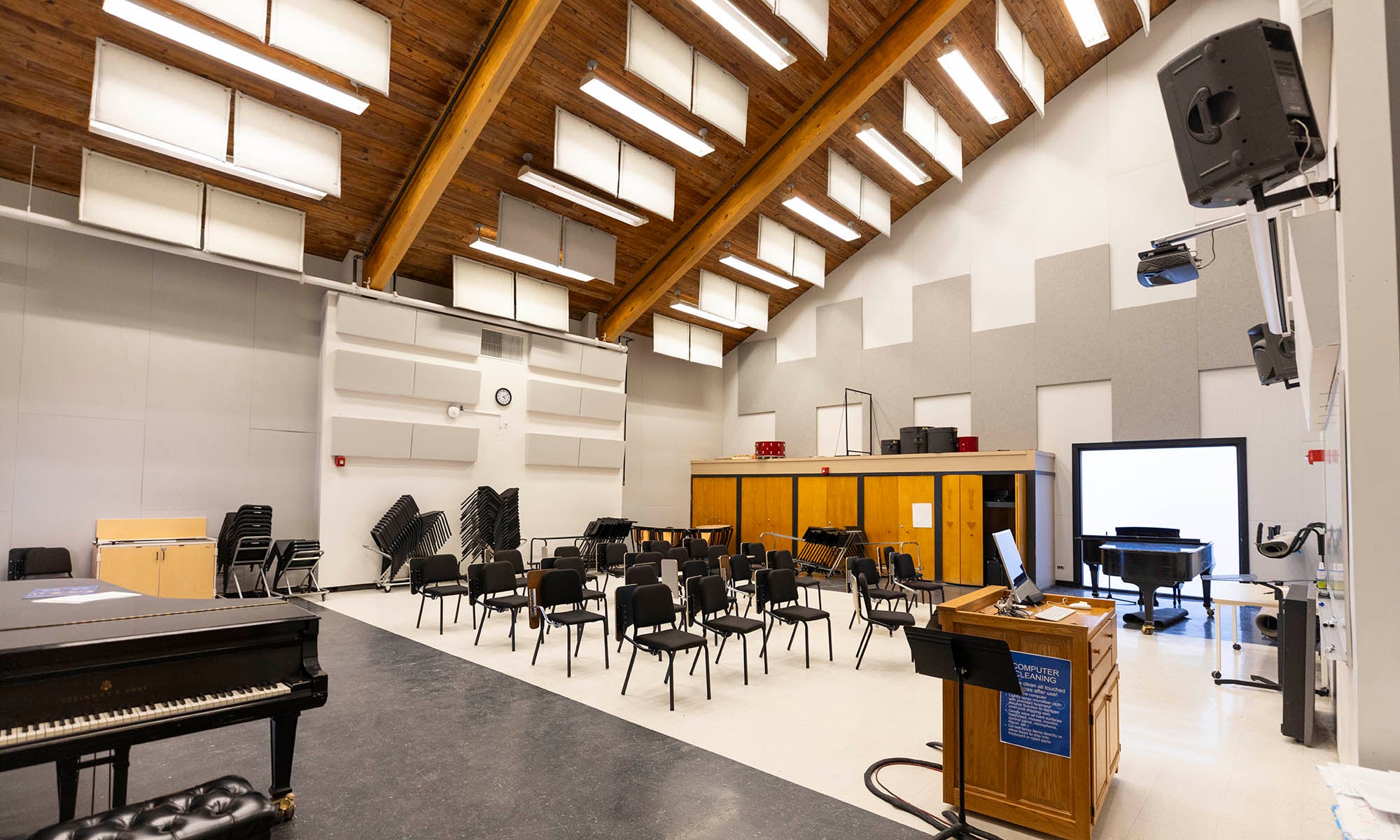 Music rehearsal space filled with chairs, a piano, and technical equipment under a vaulted ceiling lined with sound panels.