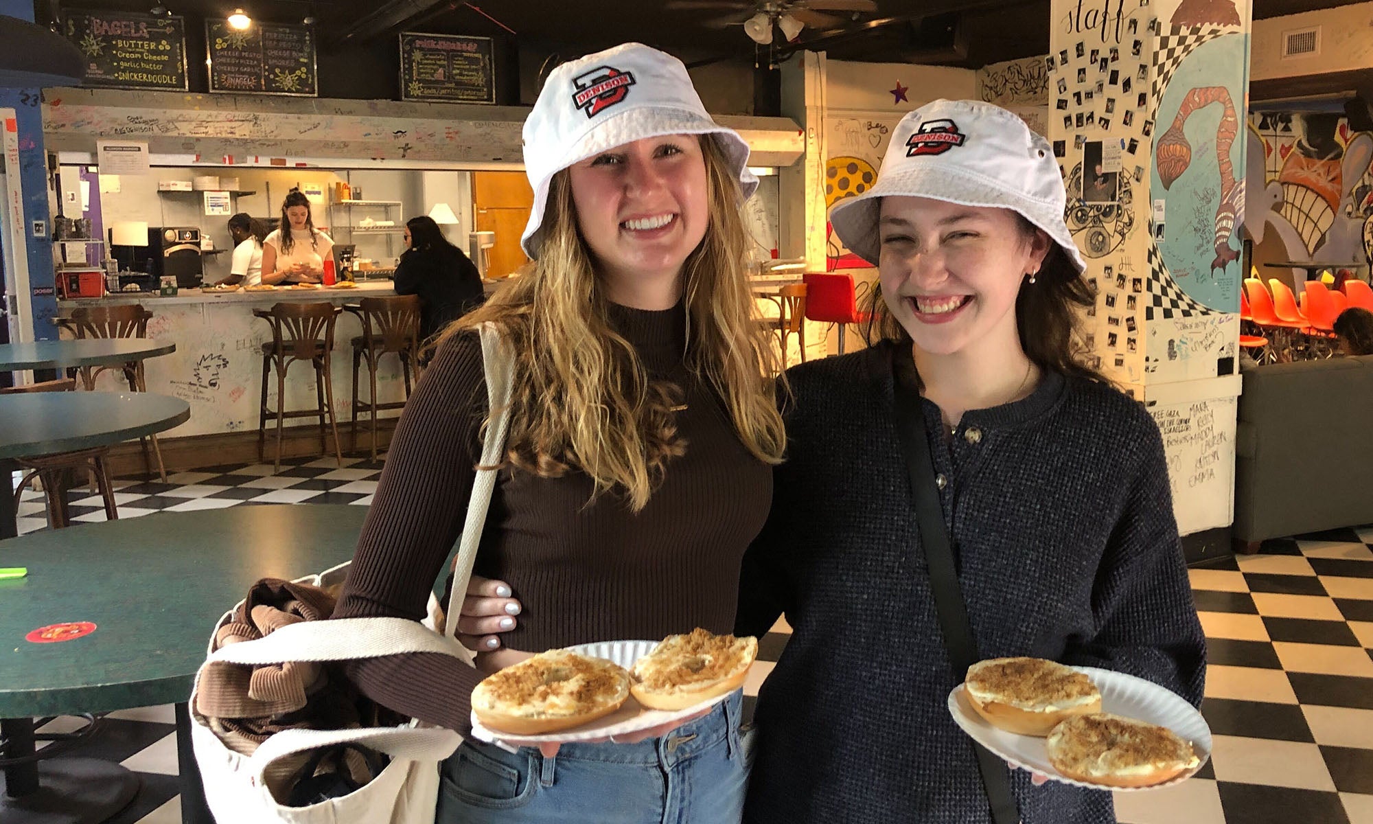 Two young women holding snagels (bagels covered in cream cheese and brown sugar) in a cafe