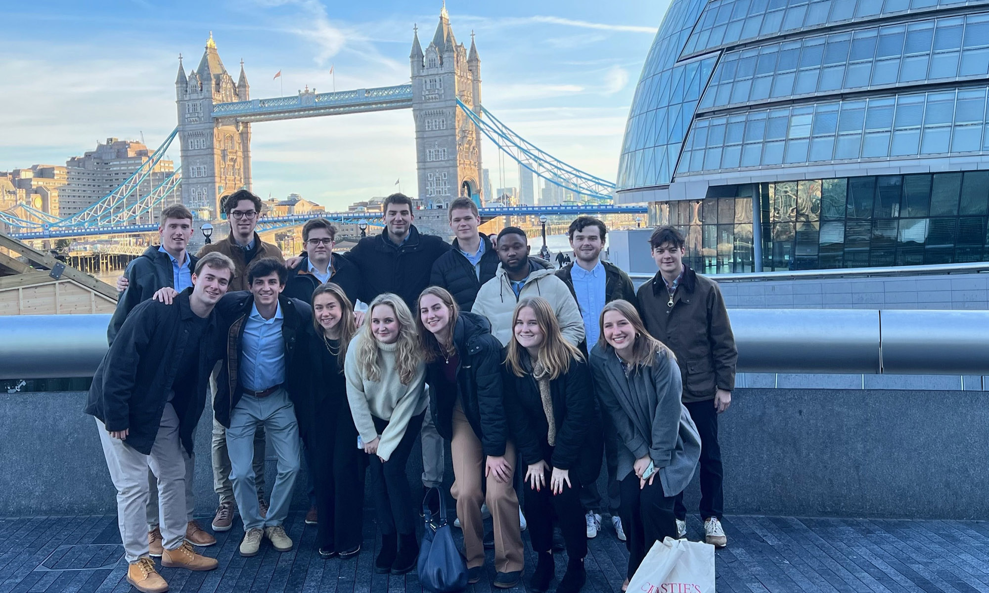 A group of people pose for a photo outdoors with Tower Bridge and a modern glass building visible in the background.