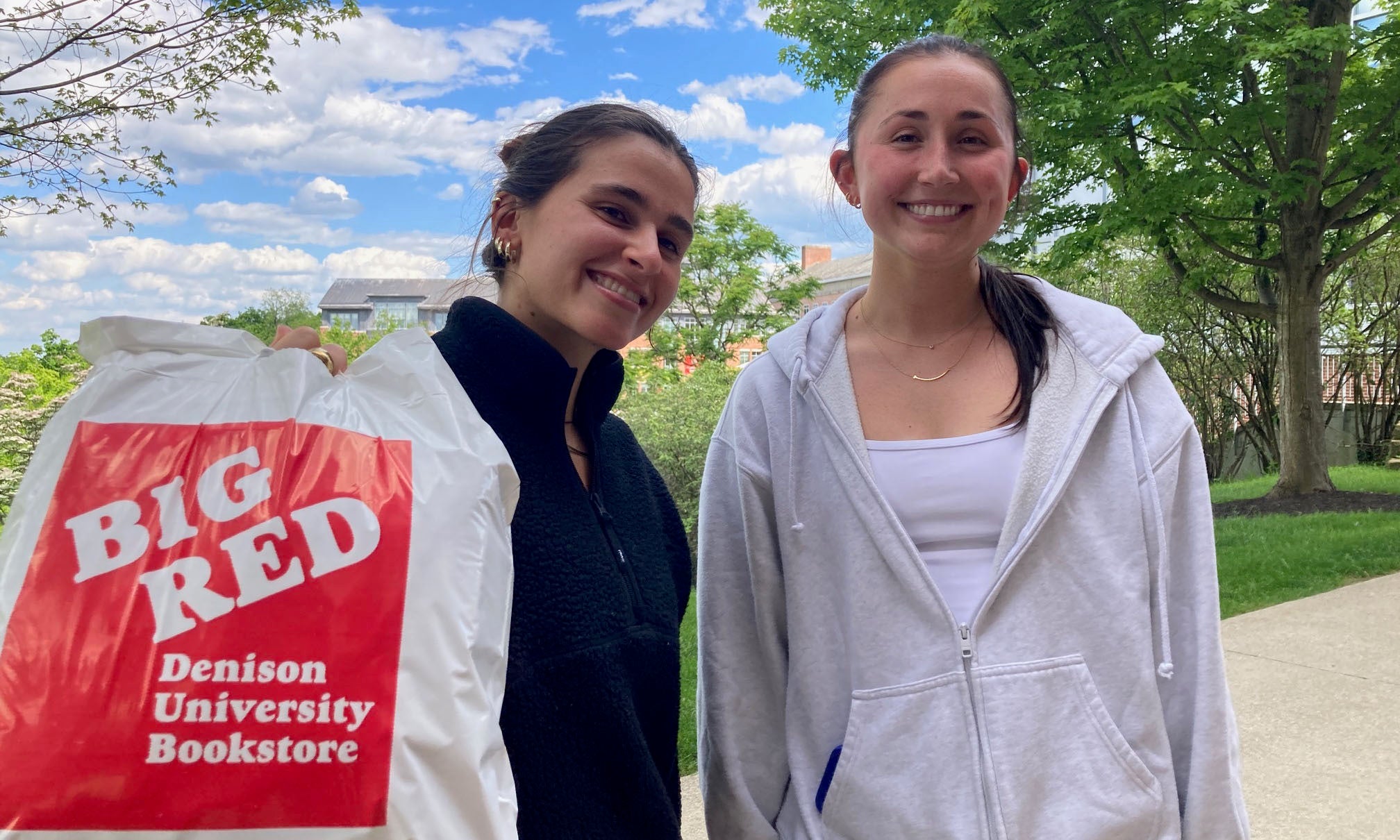 Two friends pose for a photo holding a Big Red Denison bookstore bag.