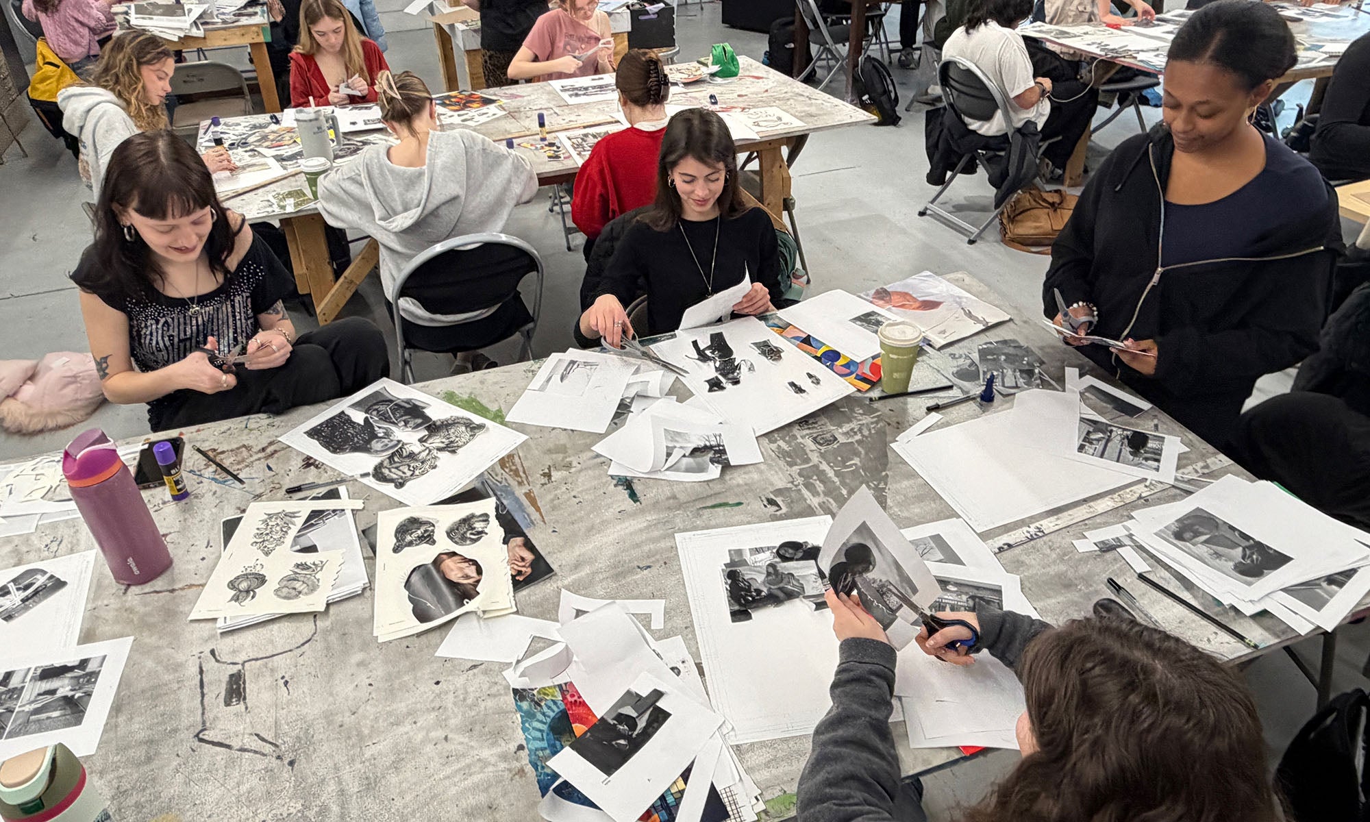 Students working on art projects around a table filled with photos and paper.