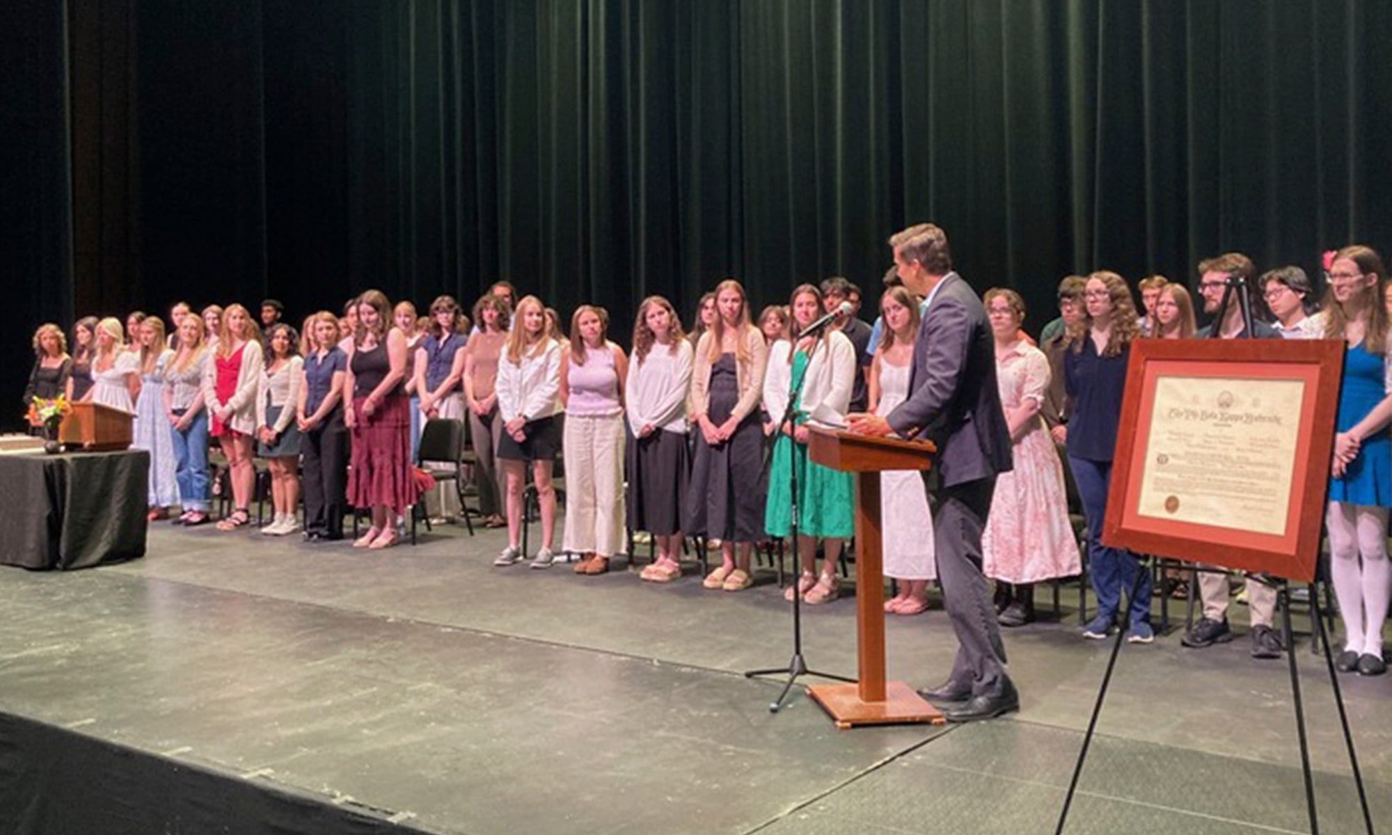 A large group of students stand on a stage during a ceremony.