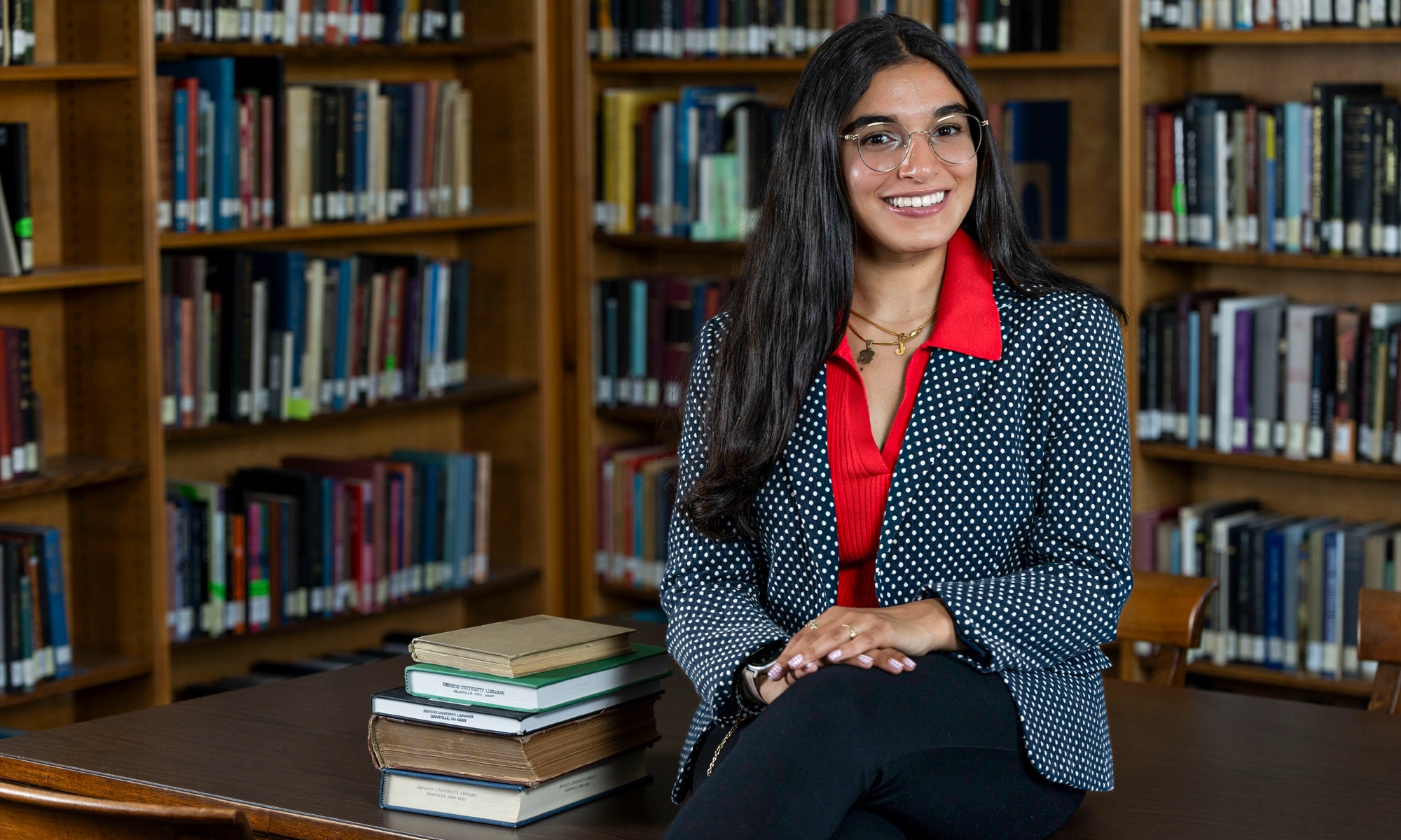 Josephine Taub smiles as she sits on a table next to a stack of books