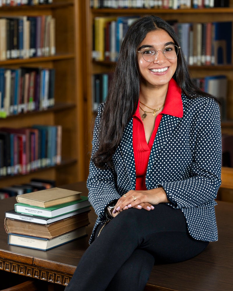 Josephine Taub smiles as she sits on a table next to a stack of books