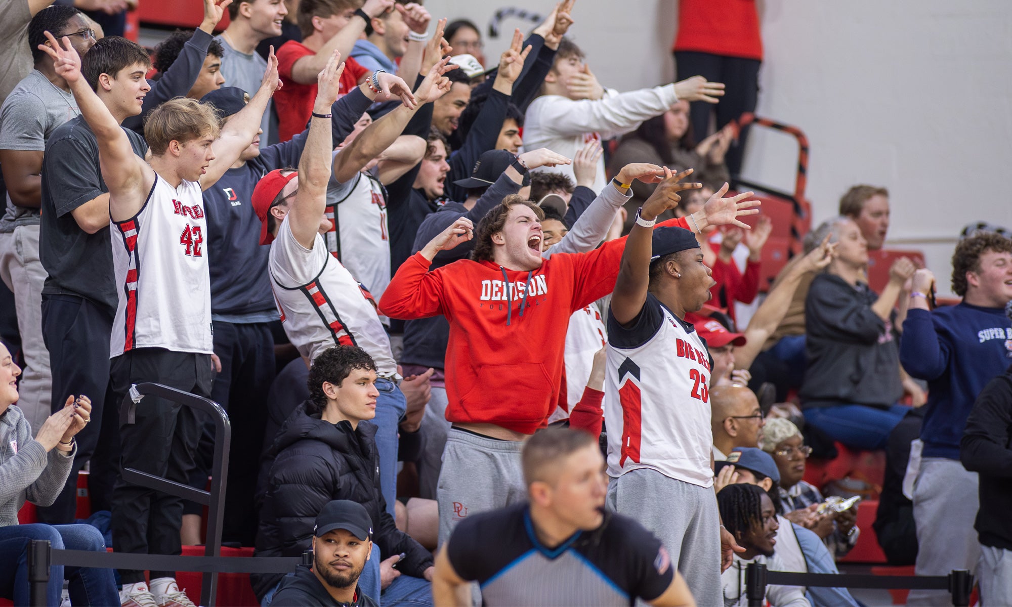 A crowd of fans in Denison gear stand and cheers on gymnasium bleachers.