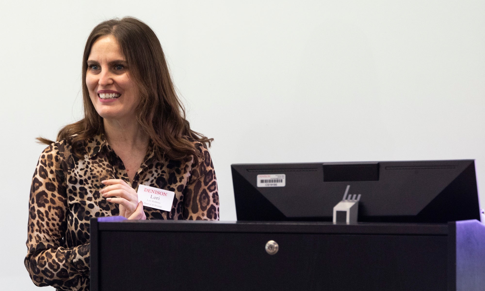 A woman stands at a podium near a computer during a presentation.