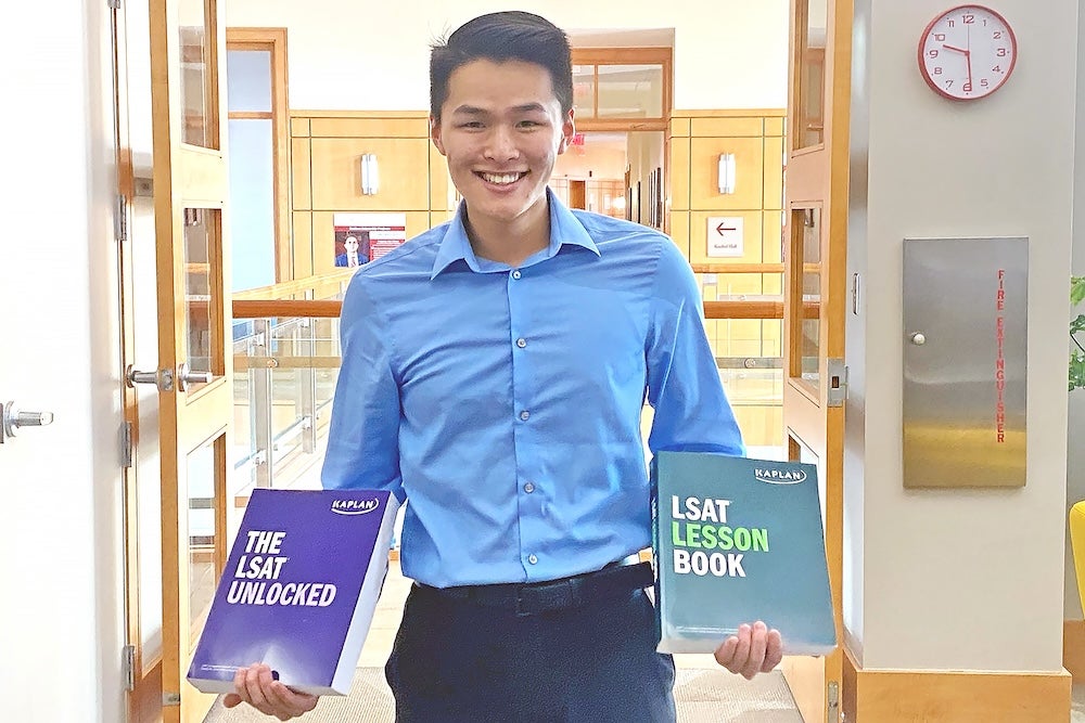 A person in a blue shirt smiles and holds two LSAT prep books