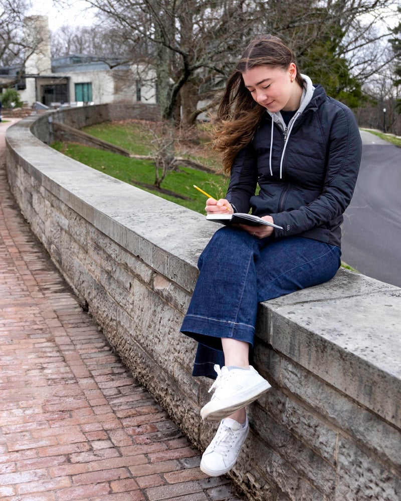 Kelsey Sweetland sits on Chapel Walk writing on a notepad