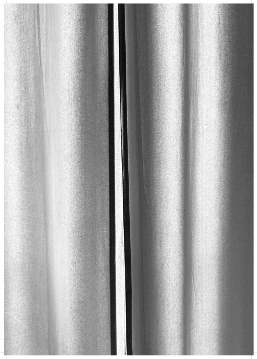 A close-up of silver metallic curtains with a narrow vertical gap in the center, showing light and shadow on the fabric.