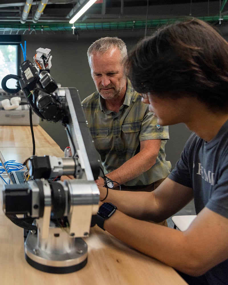 Two people work together on assembling or adjusting a robotic arm at a table in a modern lab setting.