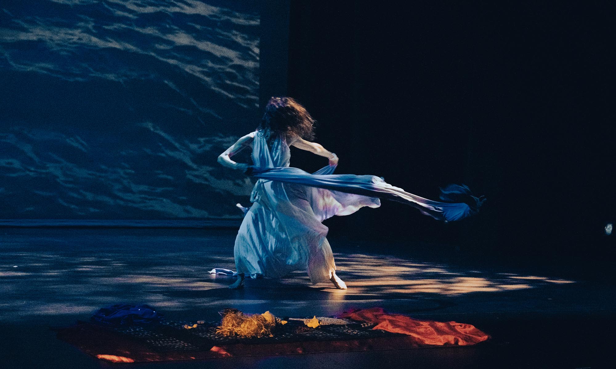A dancer in white flowing fabric dances on a blue-hued stage.