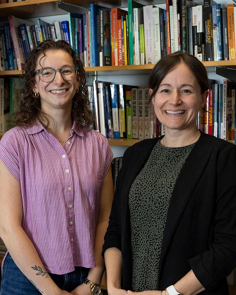 Two women pose for a photo in front of a large bookcase filled with books.
