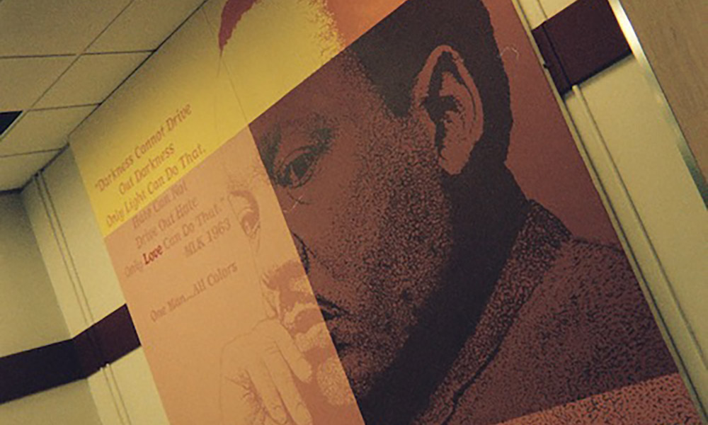 A mural on a wall features a large portrait of Martin Luther King Jr. alongside an inspirational quote, in a hallway with white and maroon walls.