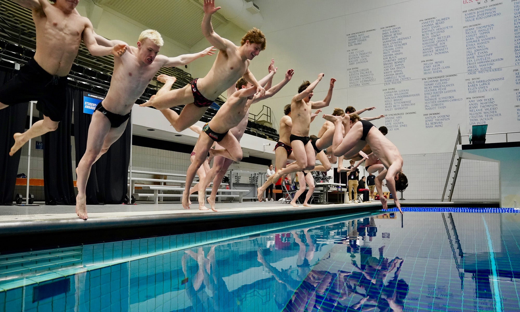 A group of more than a dozen swimmers leap into a pool in celebration.