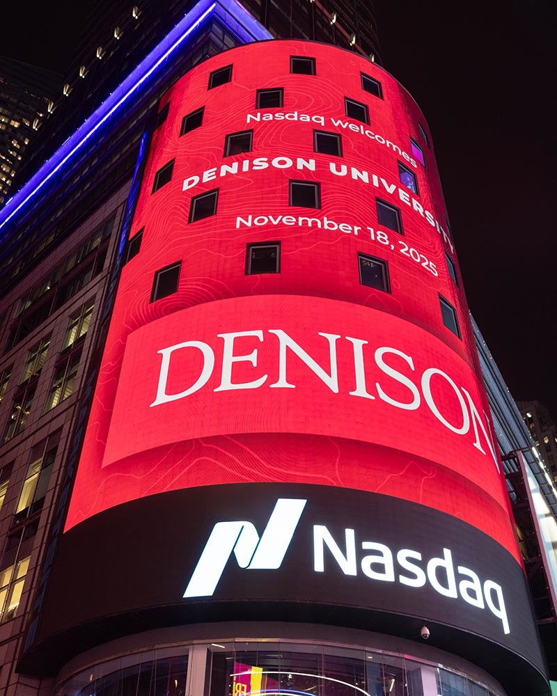 A large electronic billboard displays Denison University, November 18, 2021, DENISON in red and white above the Nasdaq logo in Times Square at night.