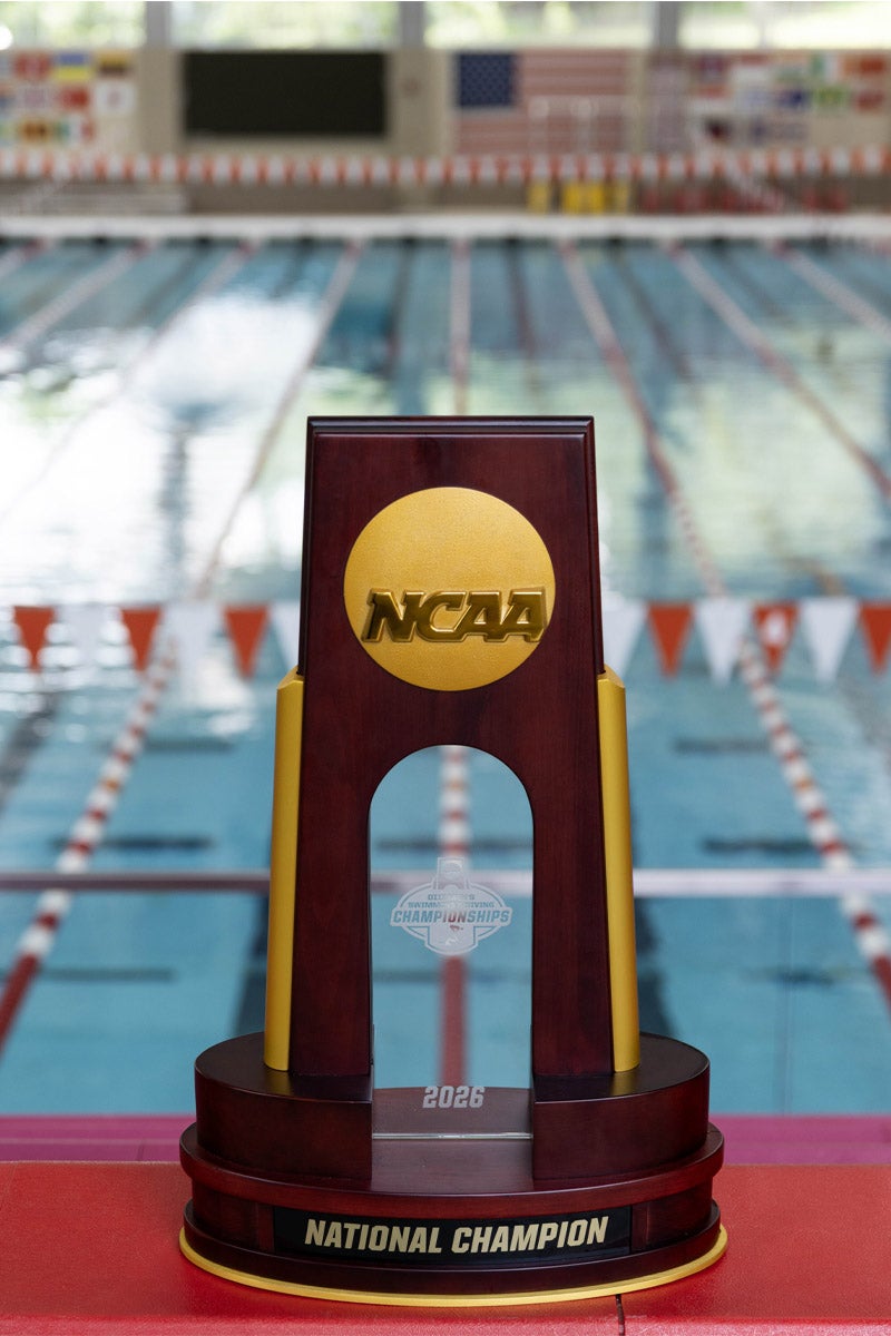An NCAA champtionship trophy centered in front of a large collegiate swimming pool.