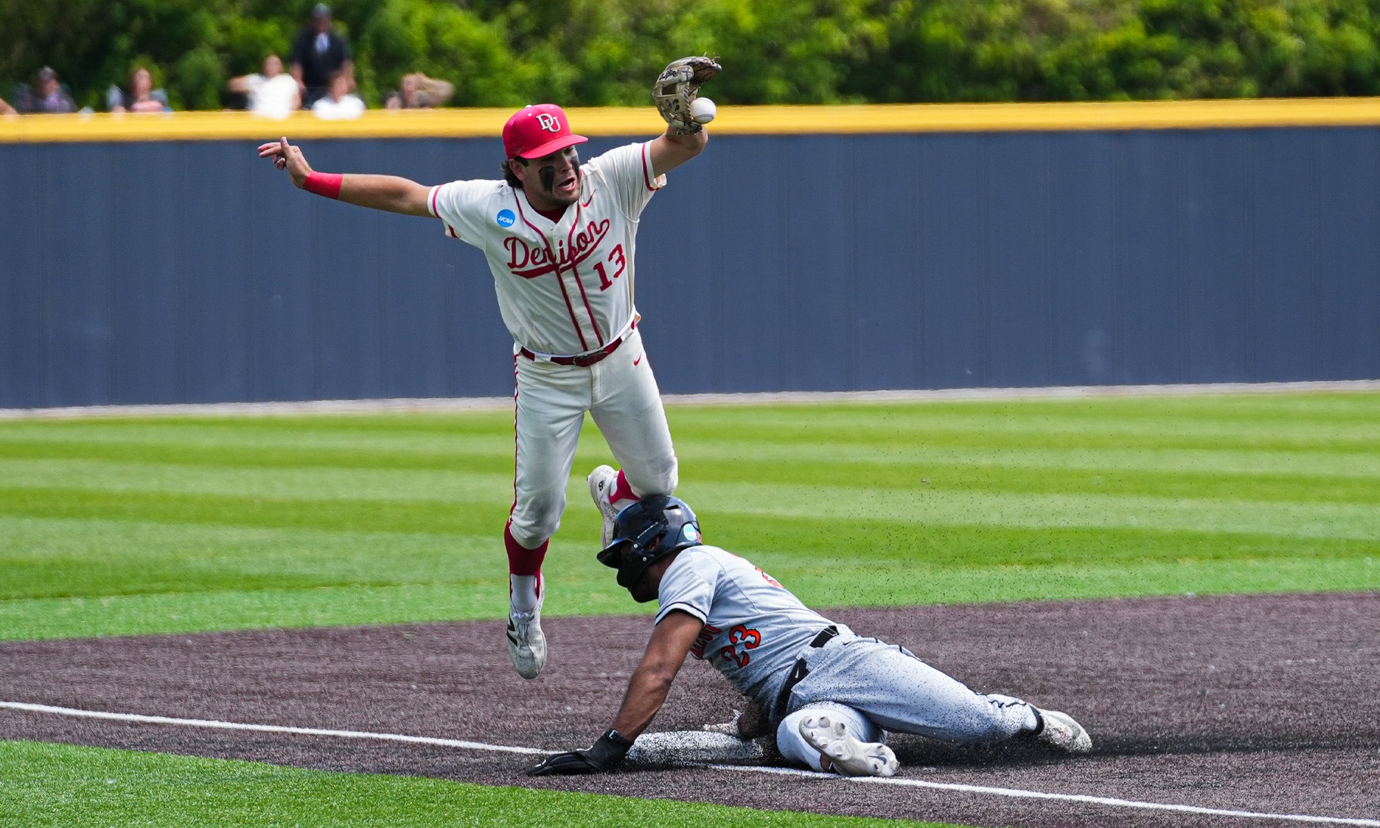 A baseball player in a white and red uniform leaps in the air as another player in a gray uniform slides safely into a base on a baseball field.
