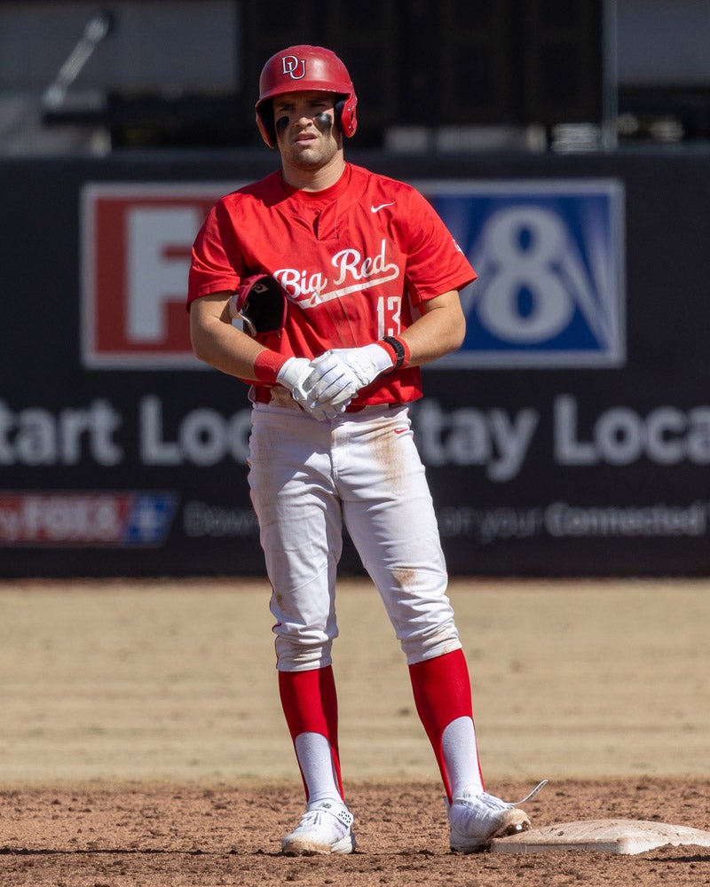 A baseball player in a red Denison uniforrm stands on base during a game.