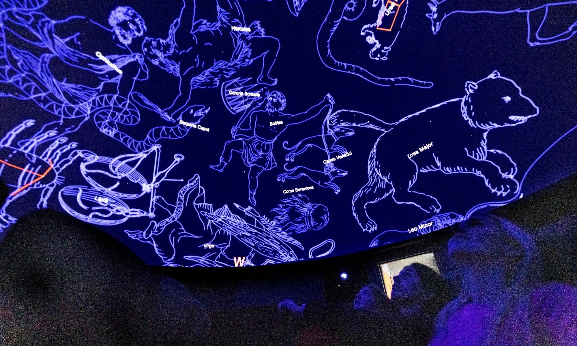A series of constellations projected on a planetarium dome above an audience.