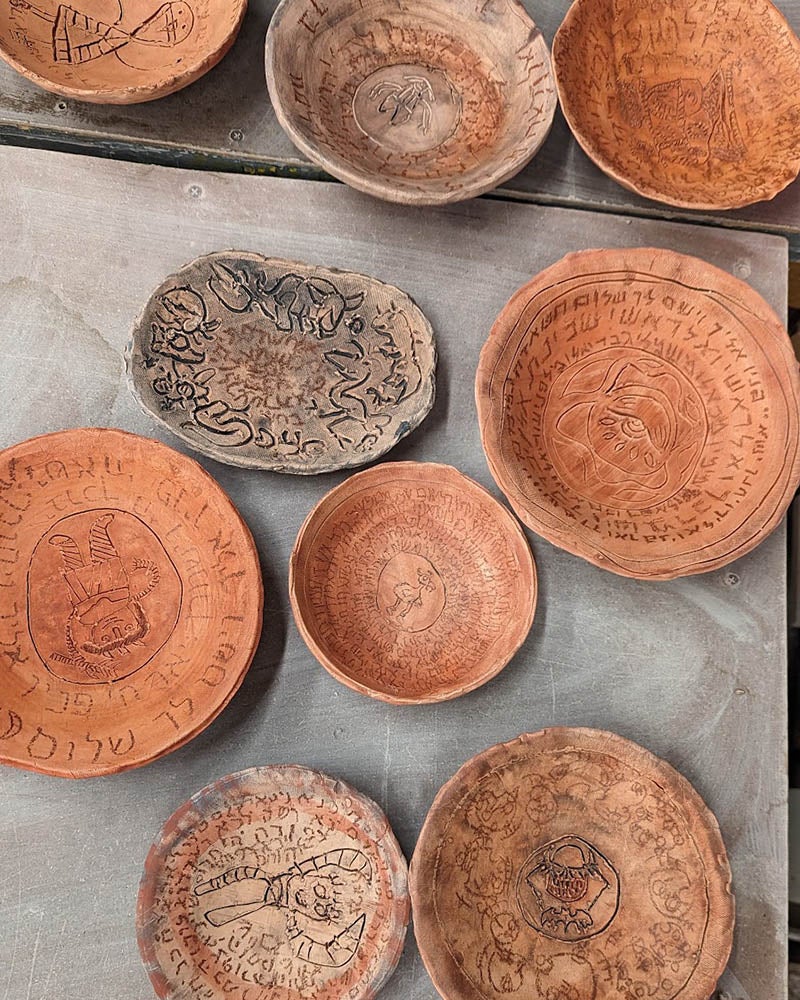 Several clay bowls, some inscribed with symbols and designs, are arranged on a flat surface. The bowls vary in size and have a rustic, reddish-brown appearance.