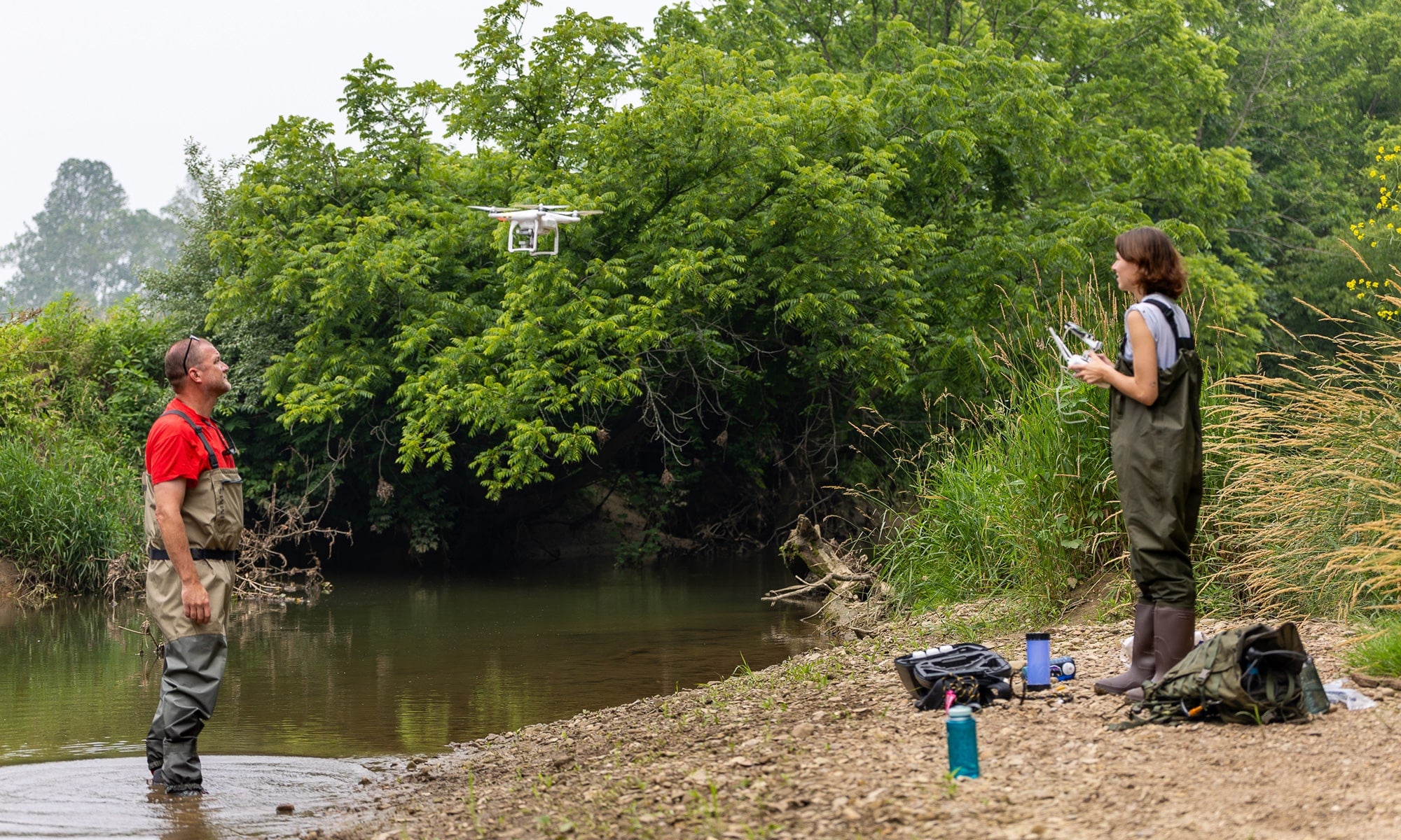 An earth sciences major flies a drone along the banks of a river as her faculty mentor watches from the shoreline.