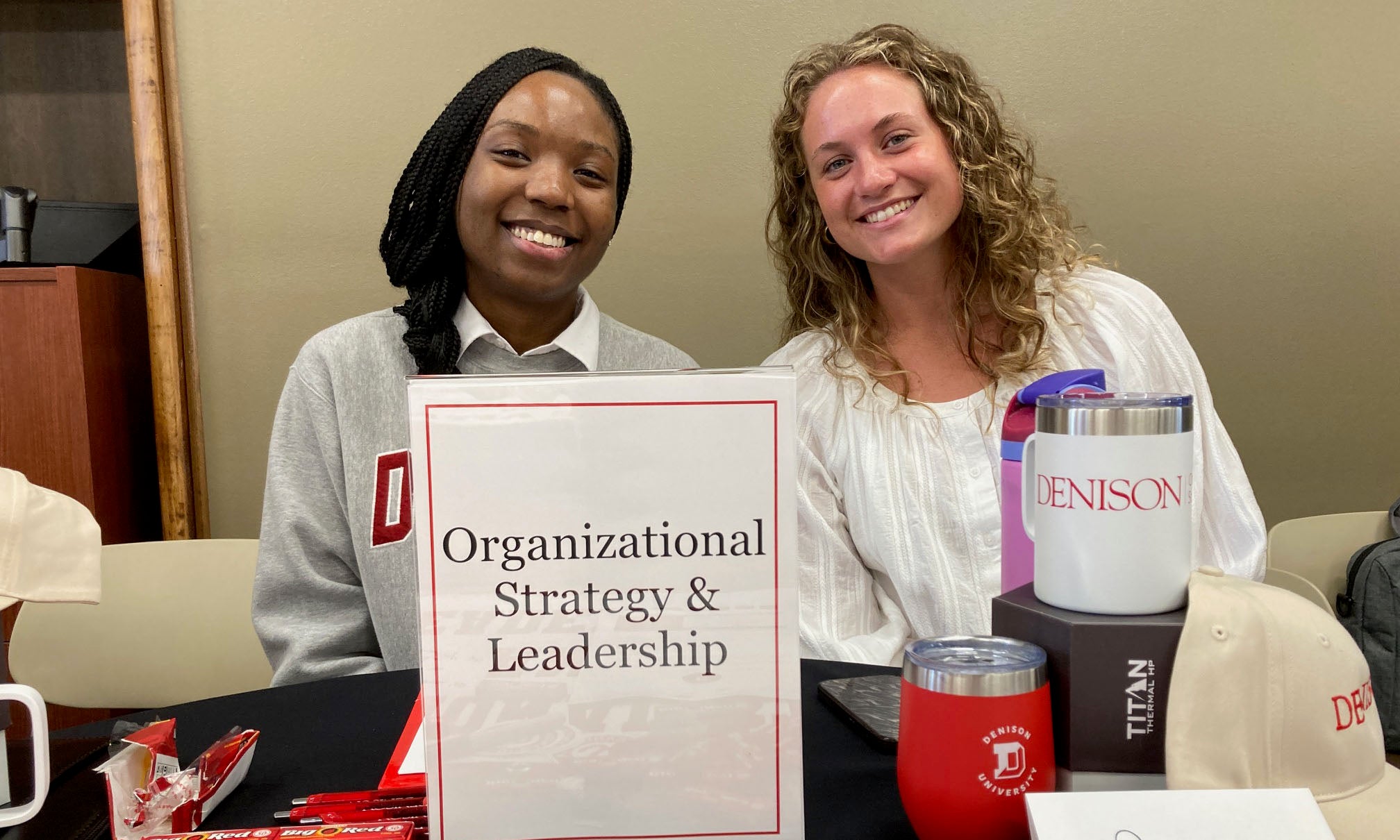 Two Organizational Strategy & Leadership students sit at their Major Day table smiling for the camera.