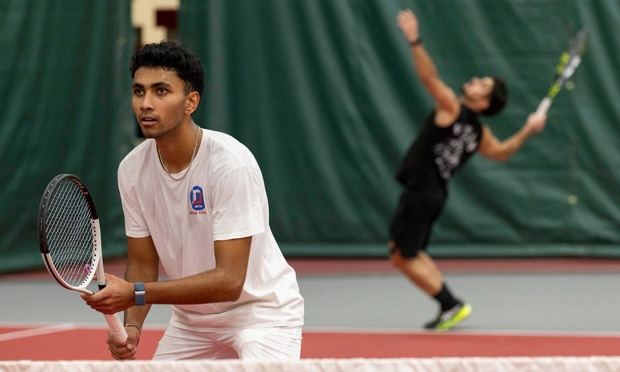 A tennis player on the court ready for a return as his doubles teammate serves in the background.