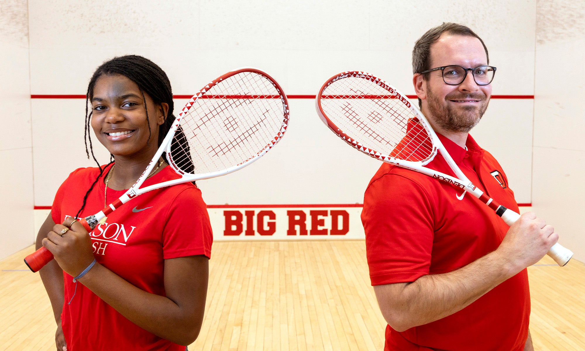 Da’Nerah Chisholm ’29 and Big Red squash coach Michael MacDonald ’09 standing on a Denison squash court in Denison athletic gear holding rackets.