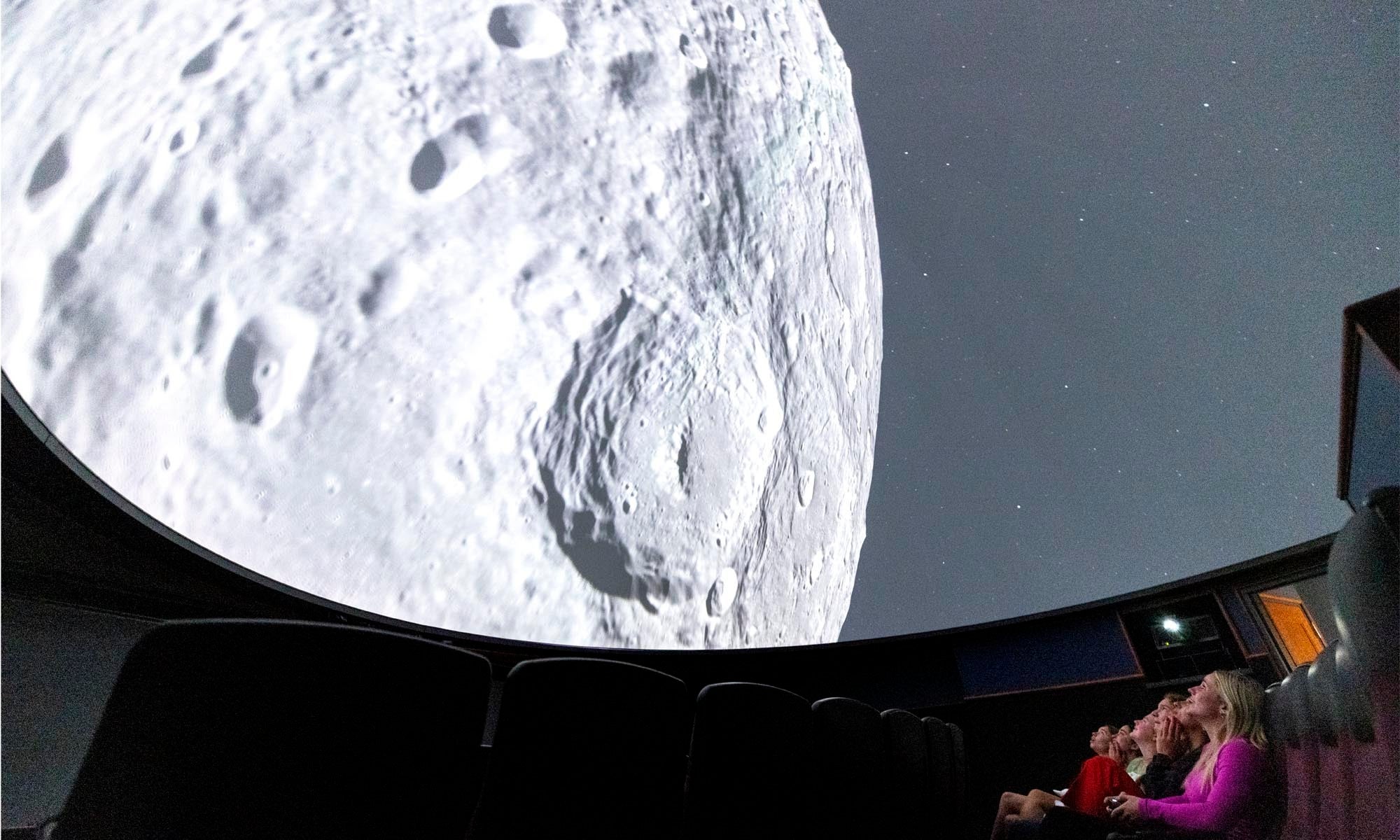 A close up view of the moon projected on a planetarium dome above an audience.