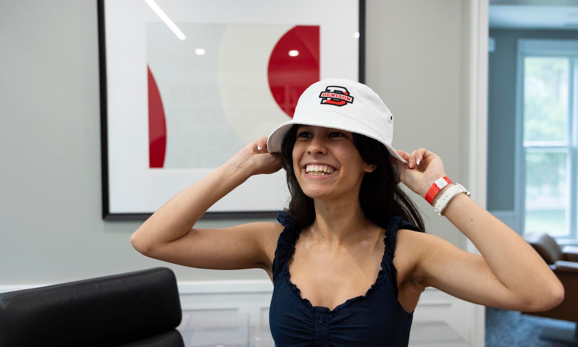 A young woman wears a white Denison boat hat and poses for a photo.