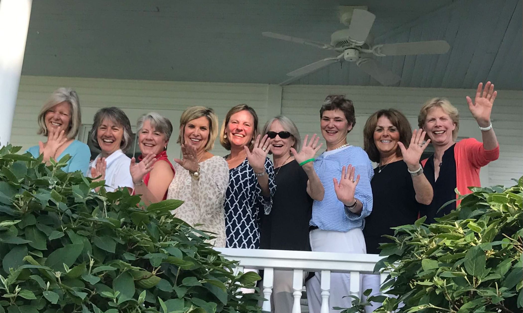 Women posing on porch waving hands