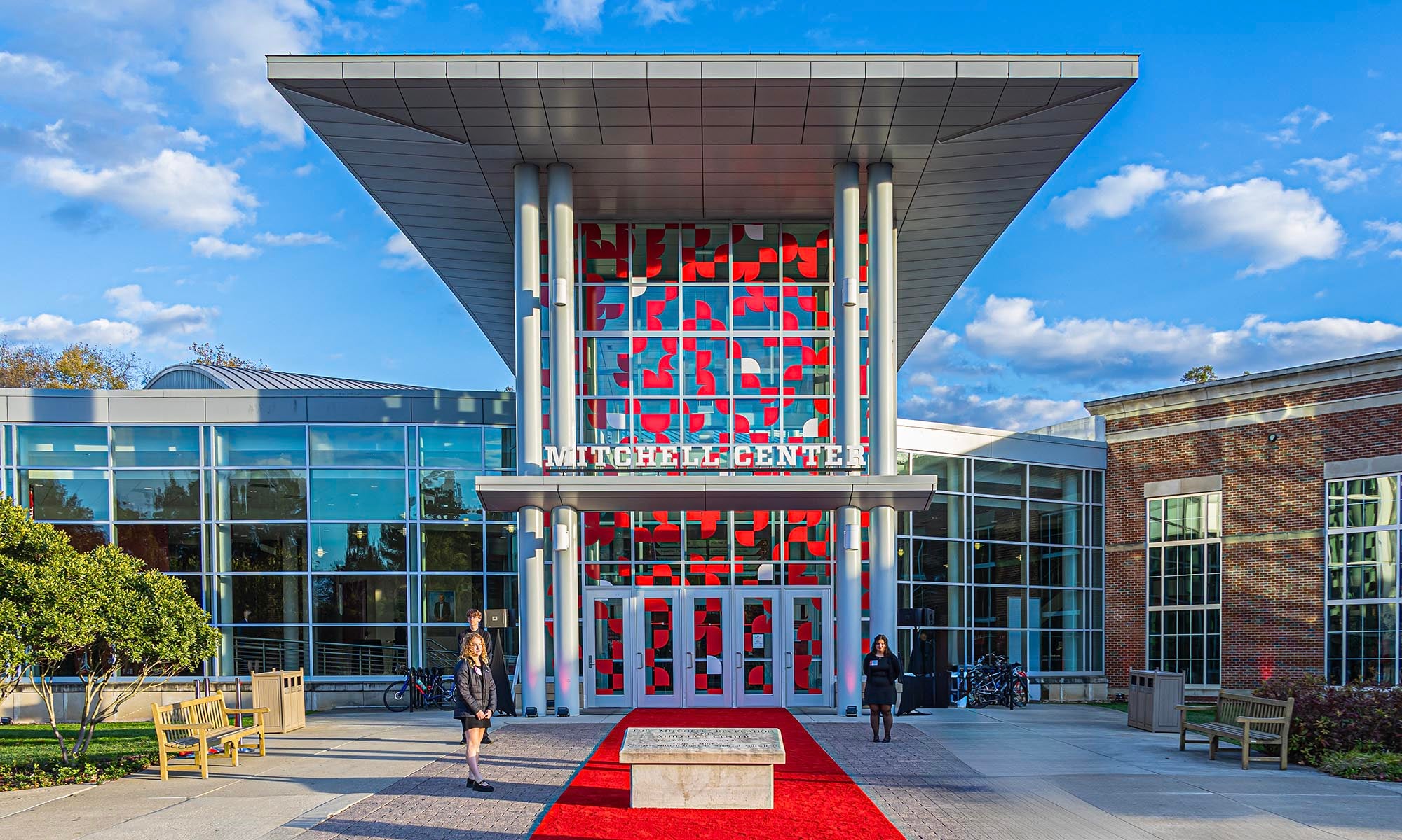 Front view of the Mitchell Recreation & Athletic Center main entrance with large glass windows, red accents, and a red carpet leading to the entrance under a modern overhang.