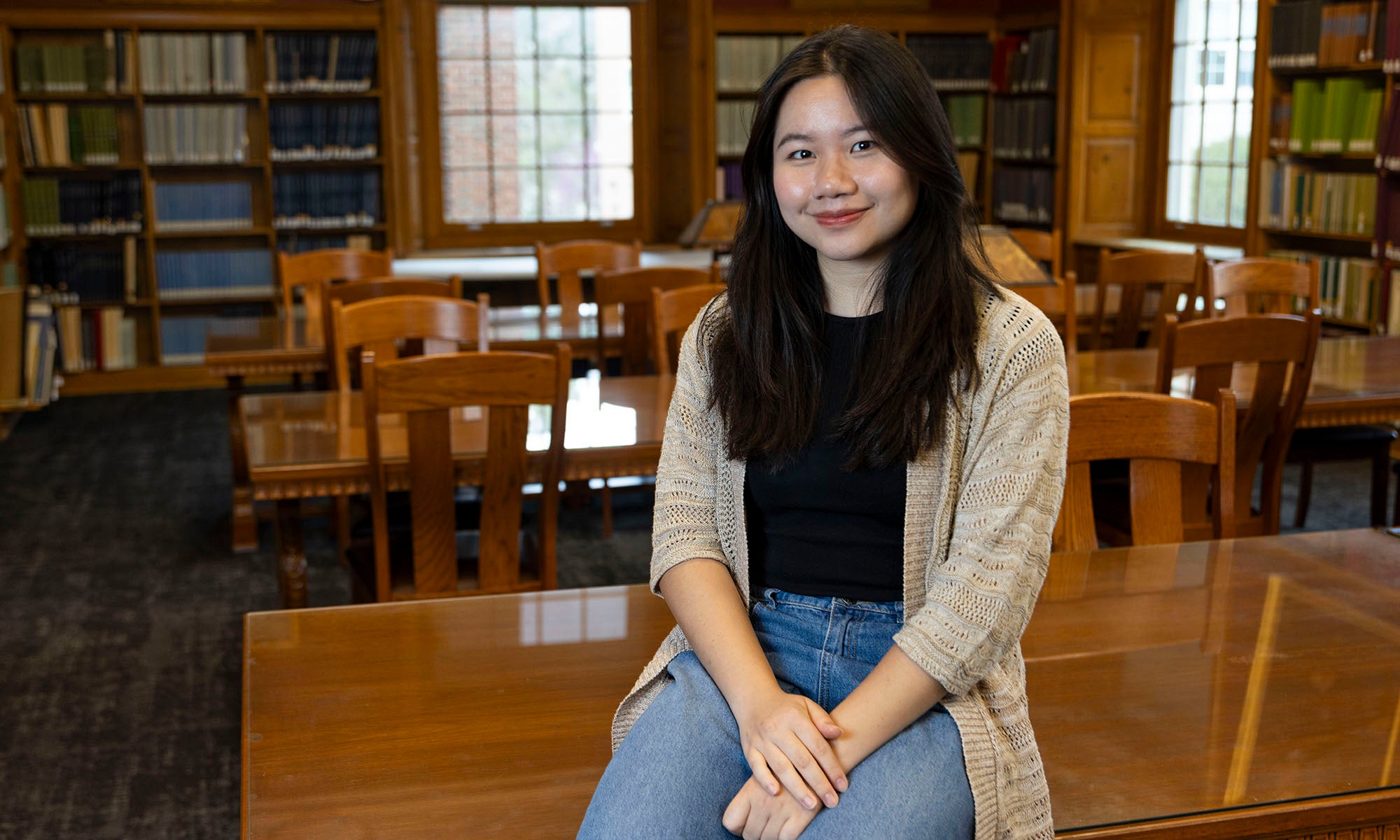 Tram Mai ‘Nancy’ Tran leaning against a wooden desk in a library.