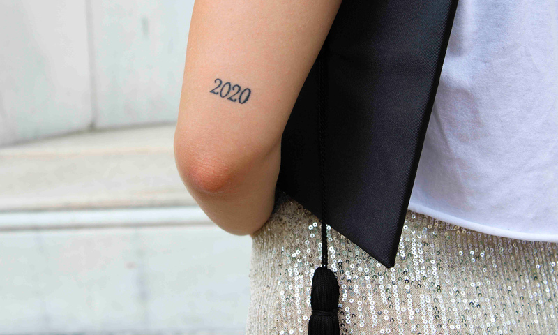 Student holding a graduation cap with a '2020' tattoo on their arm