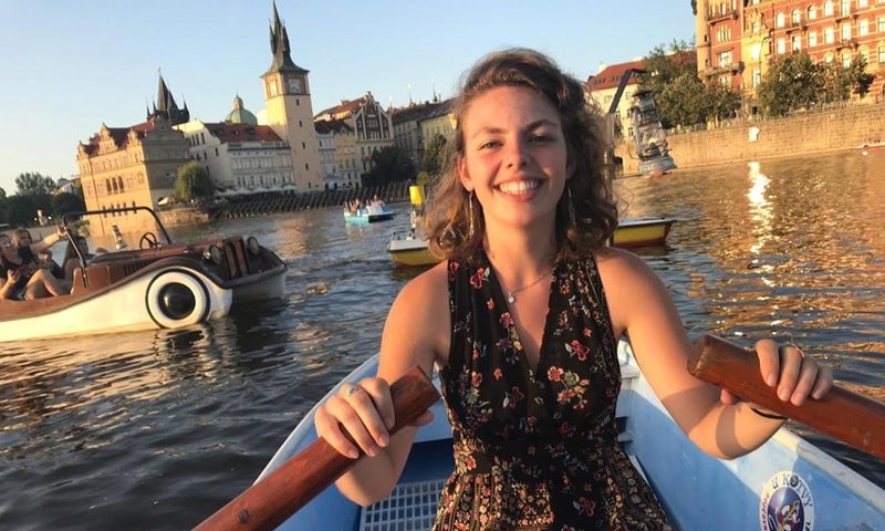 Photo of a smiling woman sitting in a row boat on, surrounded by other boaters enjoying a leisurely afternoon on a lake in Europe.