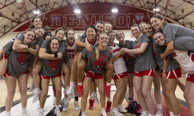 A team of collegiate women's basketball players in Denison tee shirts and shorts gathered on the court for a fun group photo.