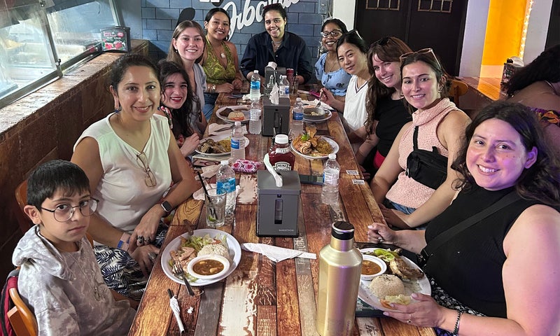 Nearly a dozen people sitting around a long wooden table filled with plates of food at a casual restaurant.