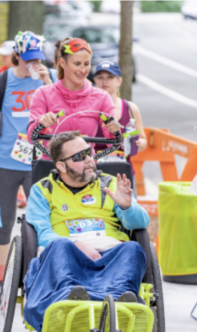rista Lehde ’06 pushes Travis Sauerwald in a racing wheelchair at the 2018 Boston Marathon Jimmy Fund Walk. He had lost mobility in the left side of his body due to a tumor on his brainstem, so his Team Wolverine took turns pushing him through all 26.2 miles. 