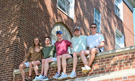 Five men sitting on a brick ledge smiling