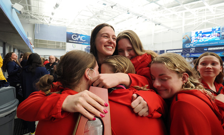 Denison swim and dive team members hugging while once clutches a trophy.