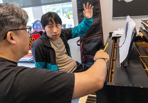  Rumi Kang ’26 sits at a piano discussing his concerto with award-winning composer Professor Ching-chu Hu. 