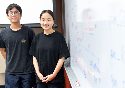 Photo of two Denison students Huy Phan and Linh Bui stand next to a dry-erase board filled with observations and notes.