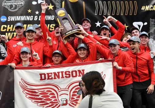 Denison swim and dive team celebrates on the podium with their trophy.