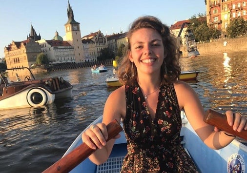 Photo of a smiling woman sitting in a row boat on, surrounded by other boaters enjoying a leisurely afternoon on a lake in Europe.