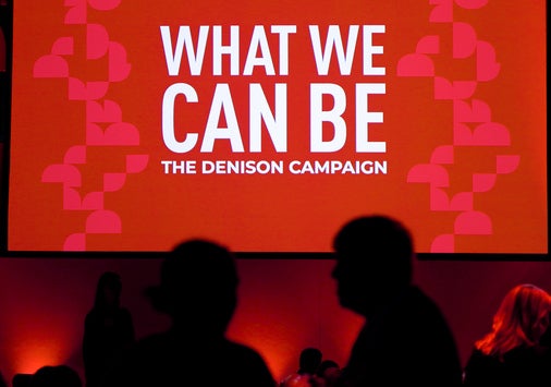 People mingle in front of a sign that says "What We Can Be."