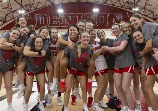 A team of collegiate women's basketball players in Denison tee shirts and shorts gathered on the court for a fun group photo.