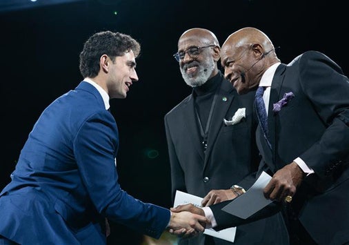 A man in a blue suit shakes hands with two men in suits as they hand him an award.