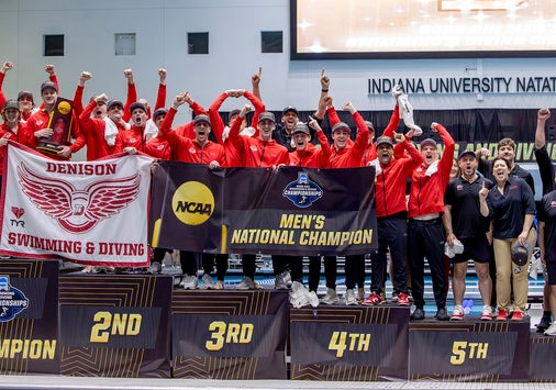 The Denison swimming and diving team celebrates on the podium poolside after winning the national championship.