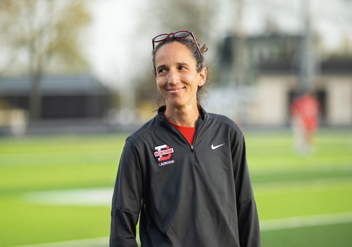 A woman with dark hair in athletic gear stands outside on a sports field.