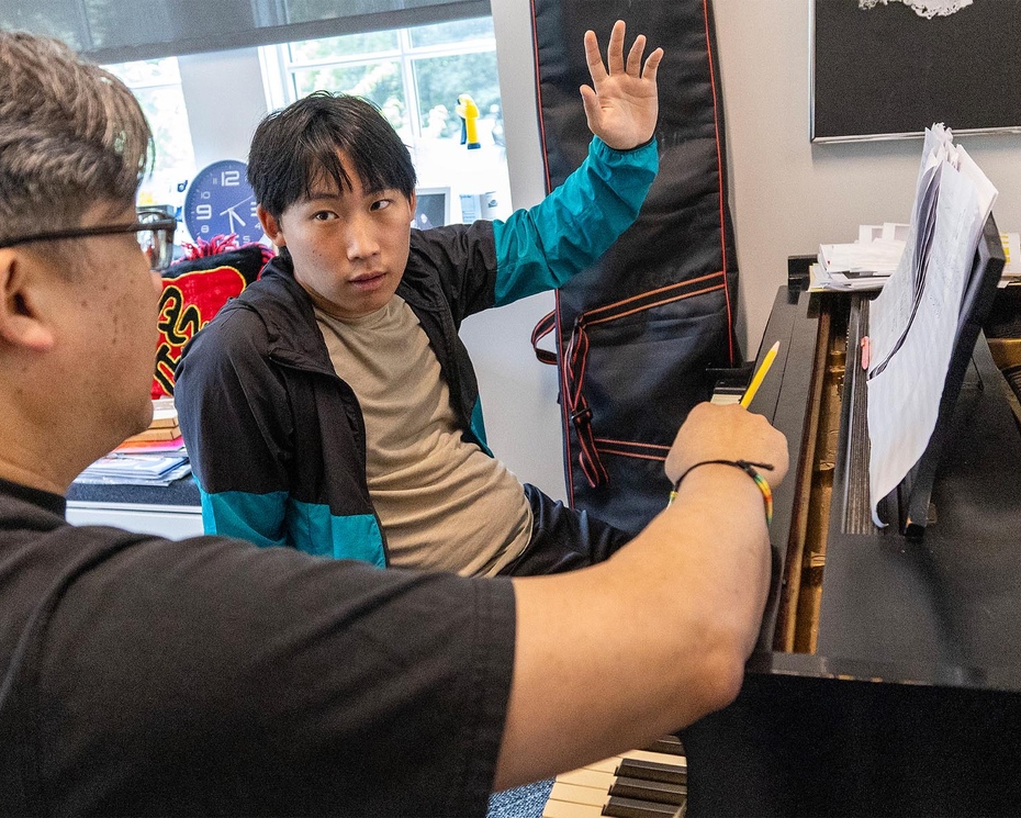  Rumi Kang ’26 sits at a piano discussing his concerto with award-winning composer Professor Ching-chu Hu. 